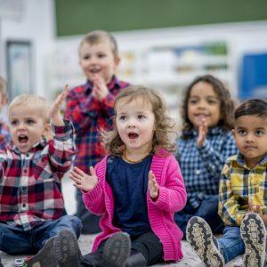 Clapping To A Song A multi-ethnic group of young children are at a preschool. They are sitting on the carpet and clapping along to music.